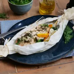 Poisson au four, savoureux et parfumé, enveloppé dans du papier sulfurisé avec des légumes et des herbes fraîches.