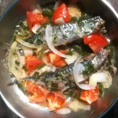 Deux maquereaux mijotent dans une poêle avec des tomates, des oignons et des herbes. Le temps de cuisson maquereau à la poêle est presque terminé.