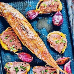Un rouget barbet rôti sur un plateau avec des toasts tartinés de rillettes, des oignons rouges et des herbes.