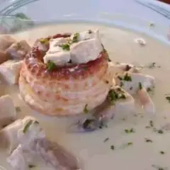 Un délicieux vol au vent aux crevettes, garni de morceaux de volaille et de persil frais, baignant dans une sauce crémeuse.