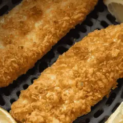 Deux filets de poisson pané dorés et croustillants, accompagnés de quartiers de citron, prêts à être dégustés dans une friteuse à air.