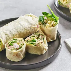 Wrap thon garni de nouilles, concombre et légumes verts, coupé en tronçons sur une assiette.