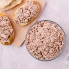 Tranches de pain garnies de rillettes de poisson, un bol rempli de rillettes de poisson et un couteau.