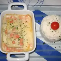 Poisson en sauce normande, parsemé de persil, servi avec une timbale de riz et une tomate cerise.
