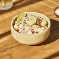 Un bol de ceviche frais, garni de rondelles de citron vert et d'oignon rouge. Une recette légère et savoureuse.