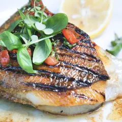Un délicieux saint pierre poisson grillé, garni de tomates et de basilic frais, servi avec un quartier de citron.