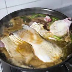 Morceaux de poisson mijotent dans une sauce matelote fumante avec des oignons et des herbes.