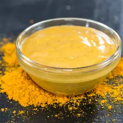 Un bol de sauce pour poisson, d'une belle couleur jaune, est posé sur un lit de poudre d'épices.