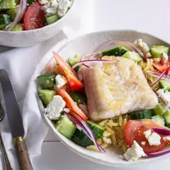 Salade de poisson méditerranéenne avec poisson blanc poêlé, concombre, tomate, oignon rouge et feta sur un lit de pâtes orzo.