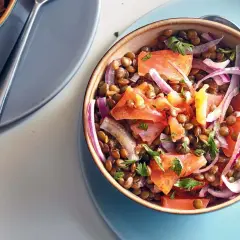 Salade de lentilles aux tomates, oignons rouges et saumon fumé, garnie de persil frais. Un plat coloré et savoureux.