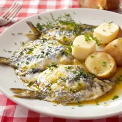 Assiette de harengs marinés avec pommes de terre et persil sur nappe à carreaux rouges.