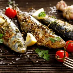 Sardines grillées, citron, tomates cerises, ail et persil sur fond de bois. Faut-il vider les sardines avant de les cuire ? La réponse est dans l'assiette !