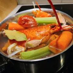Deux homards entiers mijotent dans un court-bouillon avec carottes, céleri, ail et feuille de laurier.