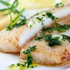 Deux filets de poisson maigre, dorés et garnis d'herbes fraîches, reposent sur une purée crémeuse. Un délice simple et savoureux.