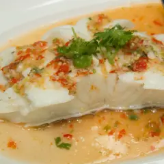 Filet de poisson blanc nappé d'une sauce épicée aux herbes et piments, rappelant un beurre blanc revisité.