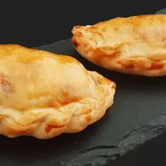 Trois chaussons dorés, un pastel thon savoureux, sur une ardoise sombre.
