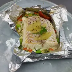 Un délicieux filet d'églefin en papillote, garni de légumes croquants et de fines tranches d'agrumes, prêt à être dégusté.