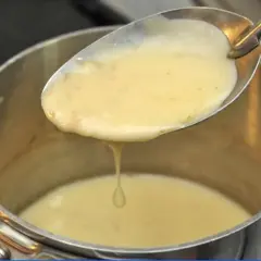 Une cuillère de sauce onctueuse, peut-être un beurre nantais, s'écoule dans une casserole.