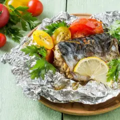 Poisson en papillote, un maquereau cuit avec des tomates et du persil, garni d'une tranche de citron.