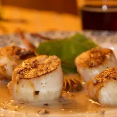 Quatre noix de Saint-Jacques poêlées, dorées et nappées d'une sauce onctueuse, sur une assiette décorée.