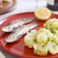 Deux sardines grillées sur une assiette rouge, accompagnées de pommes de terre persillade et d'une salade de concombre. Un vrai délice de sardine barbecue !
