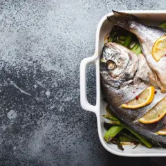 Deux saint pierre rôtis, accompagnés d'asperges, de tomates cerises et de rondelles de citron, prêts à être dégustés.