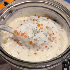 Une cuillère de sauce pour saumon crémeuse, parsemée d'aneth et de perles d'œufs de poisson, dans un bocal en verre.