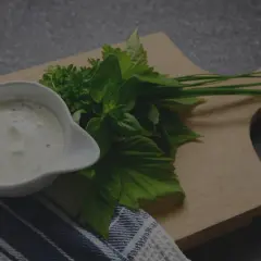 Un bol de sauce tartare crémeuse, garni d'herbes fraîches sur une planche en bois.