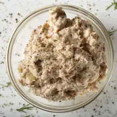 Un bol de rillettes de thon, assaisonnées de poivre noir et d'herbes, prêt à être dégusté.