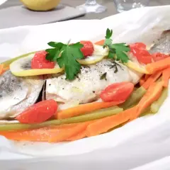 Dorade au four en papillote, garnie de tomates cerises, rondelles de citron, carottes et persil. Un plat sain et savoureux.