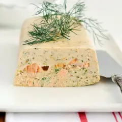Terrine de saumon frais et fumé garnie d'aneth sur une assiette blanche avec un couteau.