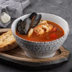 Bol de soupe de poisson aux moules et crevettes, servi avec une tranche de pain grillé et une touche de sauce rouille.