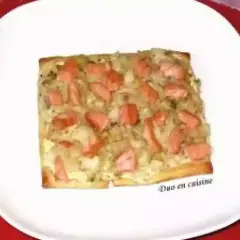 Tarte rectangulaire garnie de poireaux et de morceaux de saumon fumé, servie sur une assiette blanche.