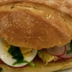 Un délicieux pan bagnat garni de tomates, œufs durs, radis et herbes fraîches. Parfait pour une recette facile et savoureuse.