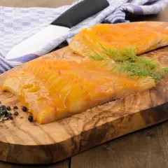 Deux beaux filets de haddock poisson fumé, prêts à être dégustés, sur une planche en bois d'olivier avec de l'aneth et du poivre.
