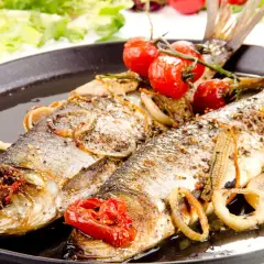 Deux poissons entiers, le hareng, rôtis avec des tomates cerises, des oignons et des rondelles de citron sur un plat noir.