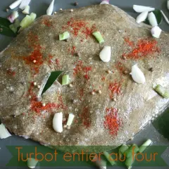 Un turbot entier est préparé pour être rôti au four, assaisonné de paprika, d'ail, d'oignons et de grains de poivre.