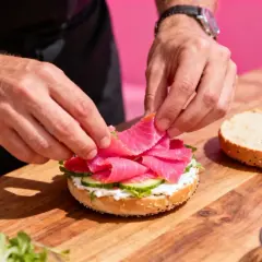 Préparation d'un bagel saumon frais avec des tranches de concombre et de la crème onctueuse.