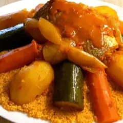 Un plat généreux de couscous garni de poisson, carottes, courgettes et pommes de terre, le tout nappé d'une sauce savoureuse.