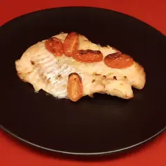 Un filet de dorade sebaste cuit, garni de tomates cerises rôties, servi sur une assiette noire.