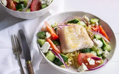 Salade de poisson méditerranéenne avec poisson blanc poêlé, concombre, tomate, oignon rouge et feta sur un lit de pâtes orzo.