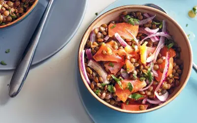 Salade de lentilles aux tomates, oignons rouges et saumon fumé, garnie de persil frais. Un plat coloré et savoureux.