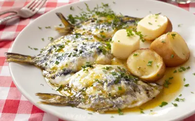 Assiette de harengs marinés avec pommes de terre et persil sur nappe à carreaux rouges.