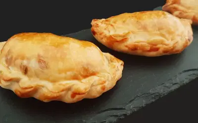 Trois chaussons dorés, un pastel thon savoureux, sur une ardoise sombre.