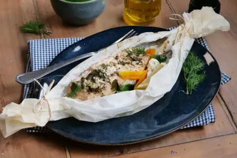 Poisson au four, savoureux et parfumé, enveloppé dans du papier sulfurisé avec des légumes et des herbes fraîches.