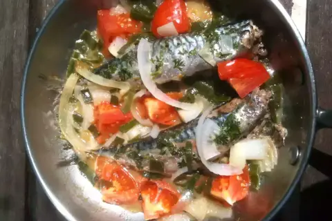 Deux maquereaux mijotent dans une poêle avec des tomates, des oignons et des herbes. Le temps de cuisson maquereau à la poêle est presque terminé.