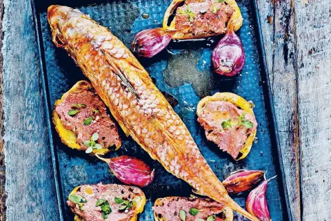 Un rouget barbet rôti sur un plateau avec des toasts tartinés de rillettes, des oignons rouges et des herbes.