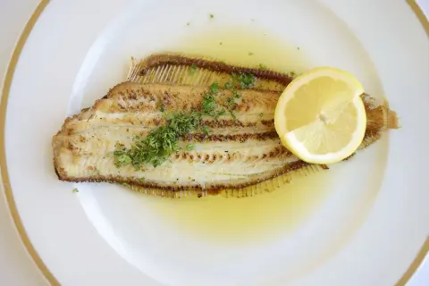 Un plat de sole meunière, un poisson délicatement poêlé, nappé d'une sauce au beurre et citron, garni de persil frais et d'une tranche de citron.