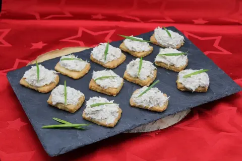 Douze toasts garnis de rillettes de maquereau, décorés d'une fine herbe verte, présentés sur une ardoise.