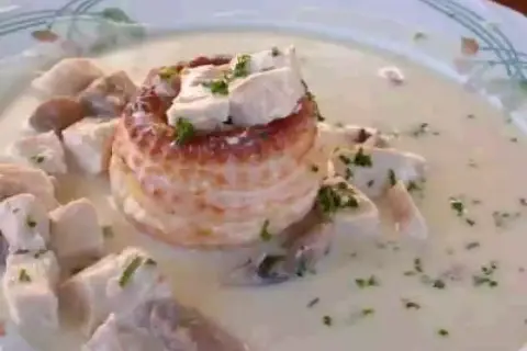 Un délicieux vol au vent aux crevettes, garni de morceaux de volaille et de persil frais, baignant dans une sauce crémeuse.